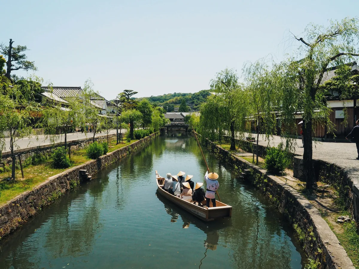 Traditioneel bootje met passagiers op het kanaal van de Bikan-wijk tussen wilgen, in Kurashiki