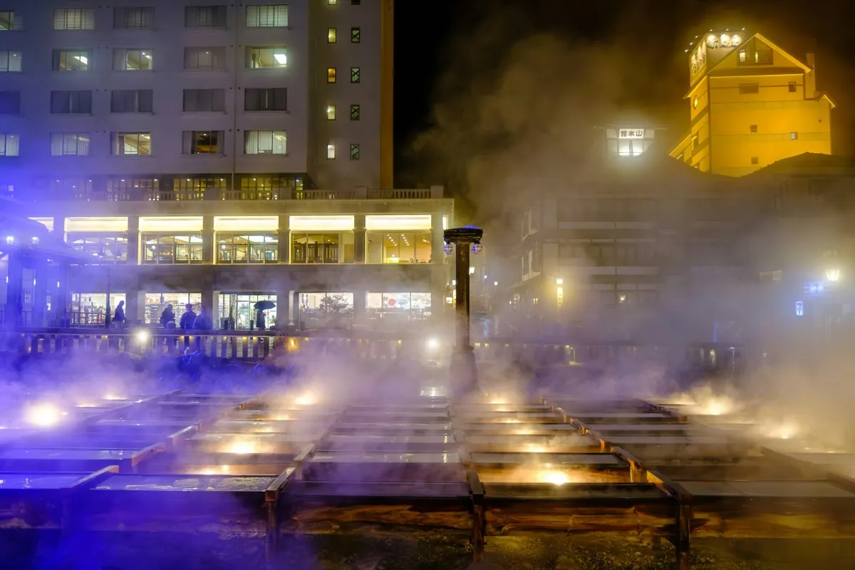 Verlichte houten kanalen van de Yubatake met stoom in Kusatsu bij nacht